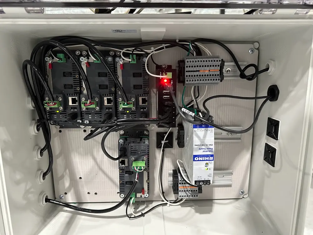 Inside a control enclosure: DIN-rail mounted scale interface modules, each with an Ethernet port and load-cell terminals, wired to terminal blocks and an industrial DC power supply.