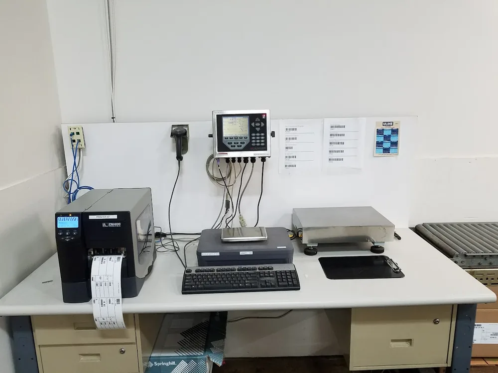 A counting and labeling workstation with a Zebra ZM400 printer, bench scale platform and wall-mounted indicator, with barcode samples posted above.