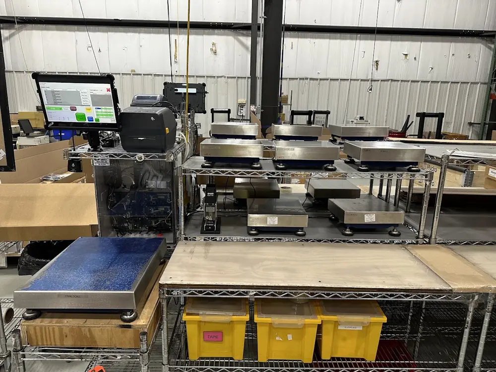 Progressive Scale negative-weighing station with scan validation at Thule: a touchscreen running the Progressive Scale interface beside a label printer and a rack of six networked counting scales, with a final-check platform in front.